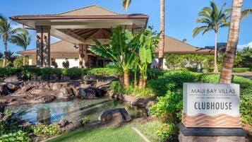 A hotel with a covered outdoor area, a pool with rocks, and palm trees.