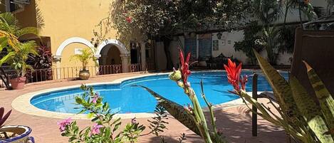 A pool surrounded by tropical plants and a yellow building.