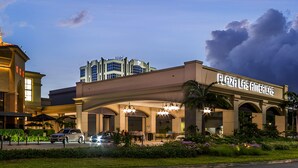 Ein Hotel mit einem gut sichtbaren Schild, auf dem „Plaza Las Americas“ steht. Es zeichnet sich durch einen modernen Baustil mit Flachdach und großen Fenstern aus. Das Gebäude wird von gepflegter Bepflanzung umgeben und verfügt über einen Parkplatz davor.
