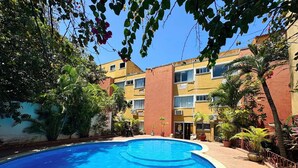 Una piscina rodeada de follaje y un edificio de varios pisos con balcones.