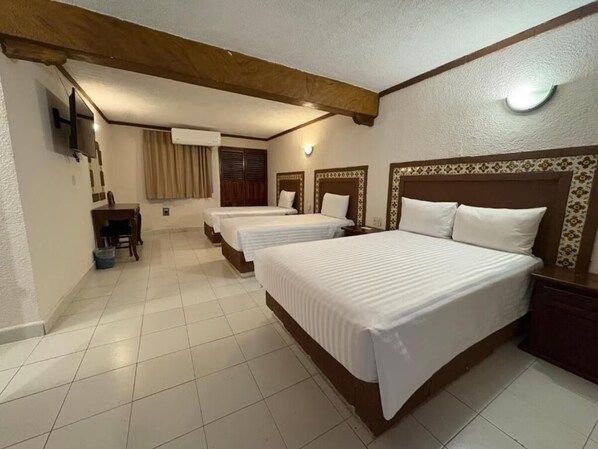 A hotel room with three beds, a TV, a desk, and a chair.