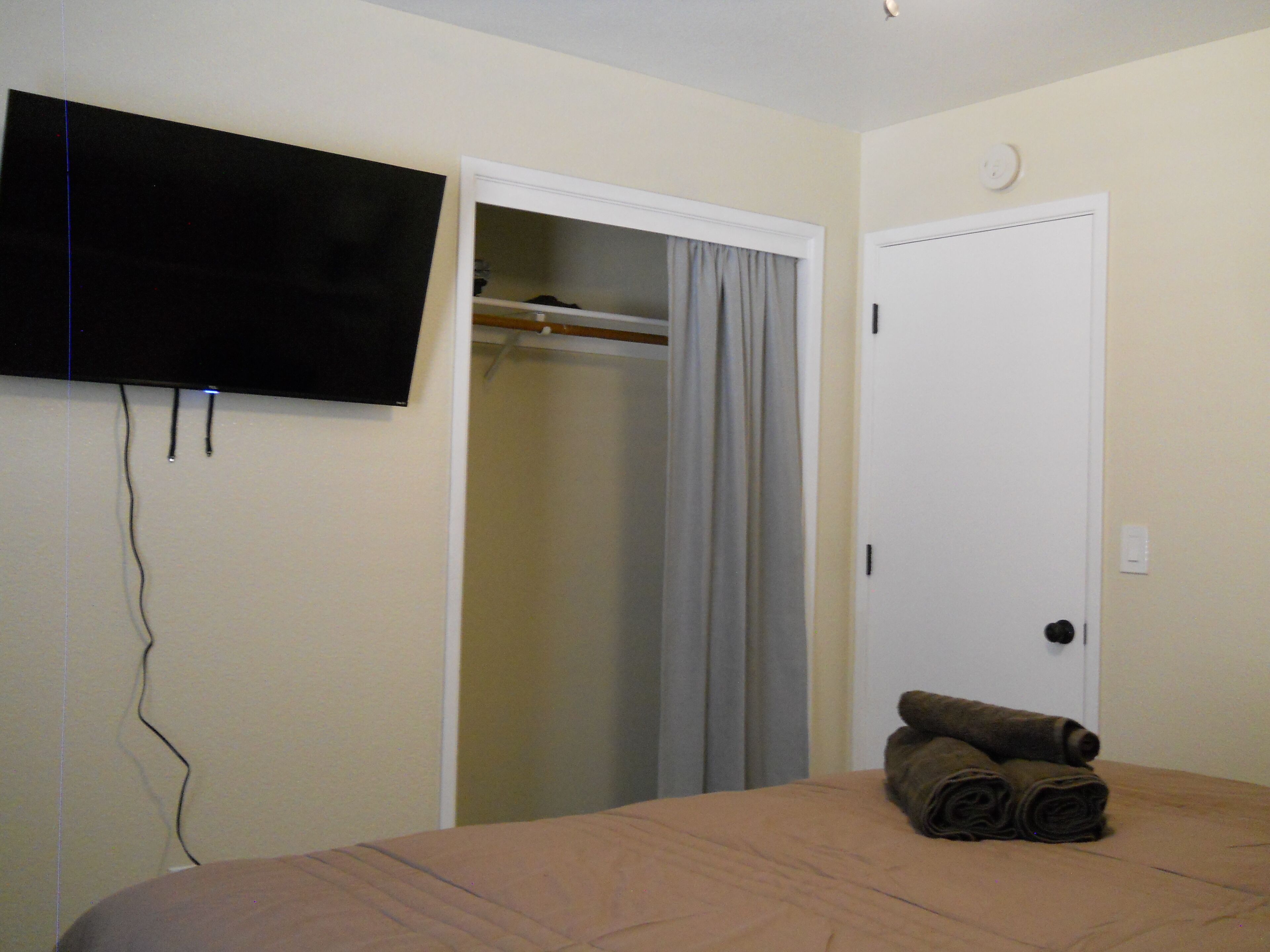A bedroom with a bed, a television mounted on the wall, a closet with a door, and a towel on the bed.