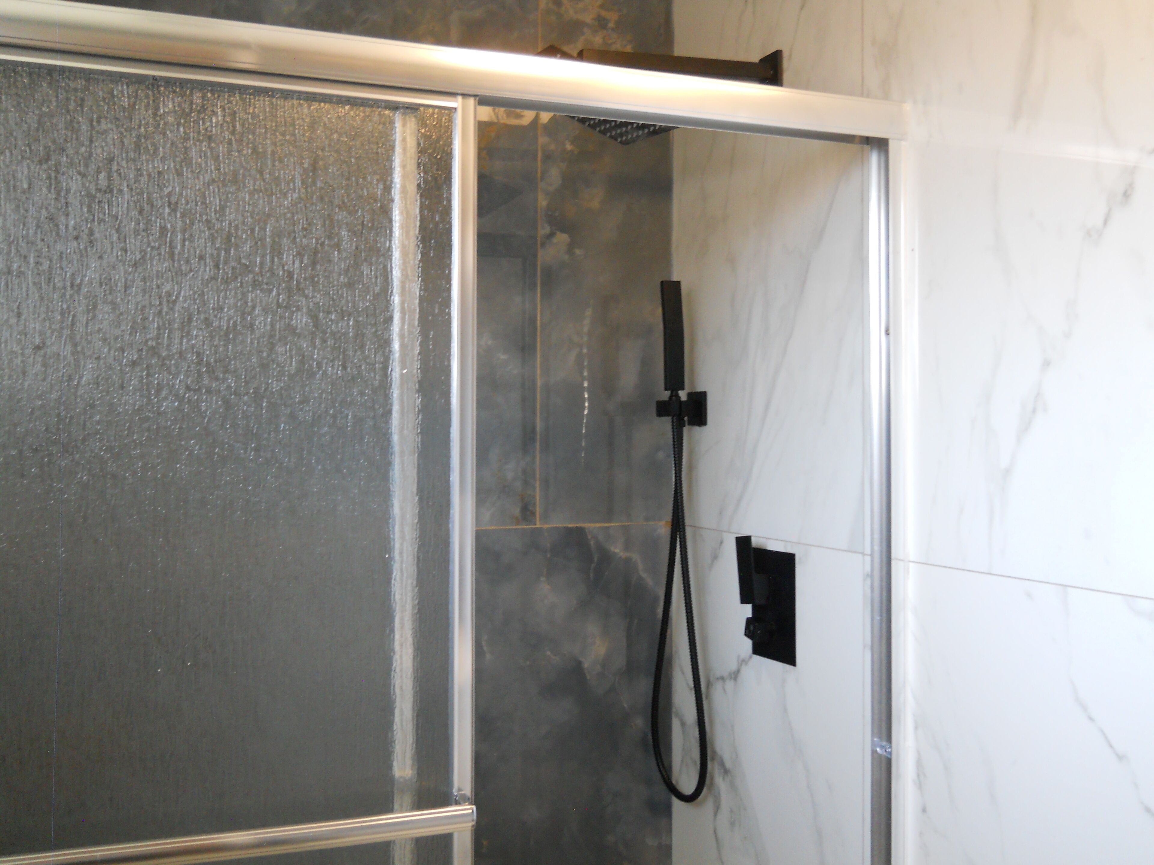 A shower enclosure with a glass door, a handheld showerhead, and a control panel on the wall.