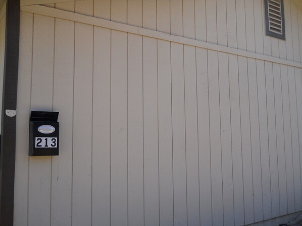 A white building with vertical siding and a black mailbox with the number 213.