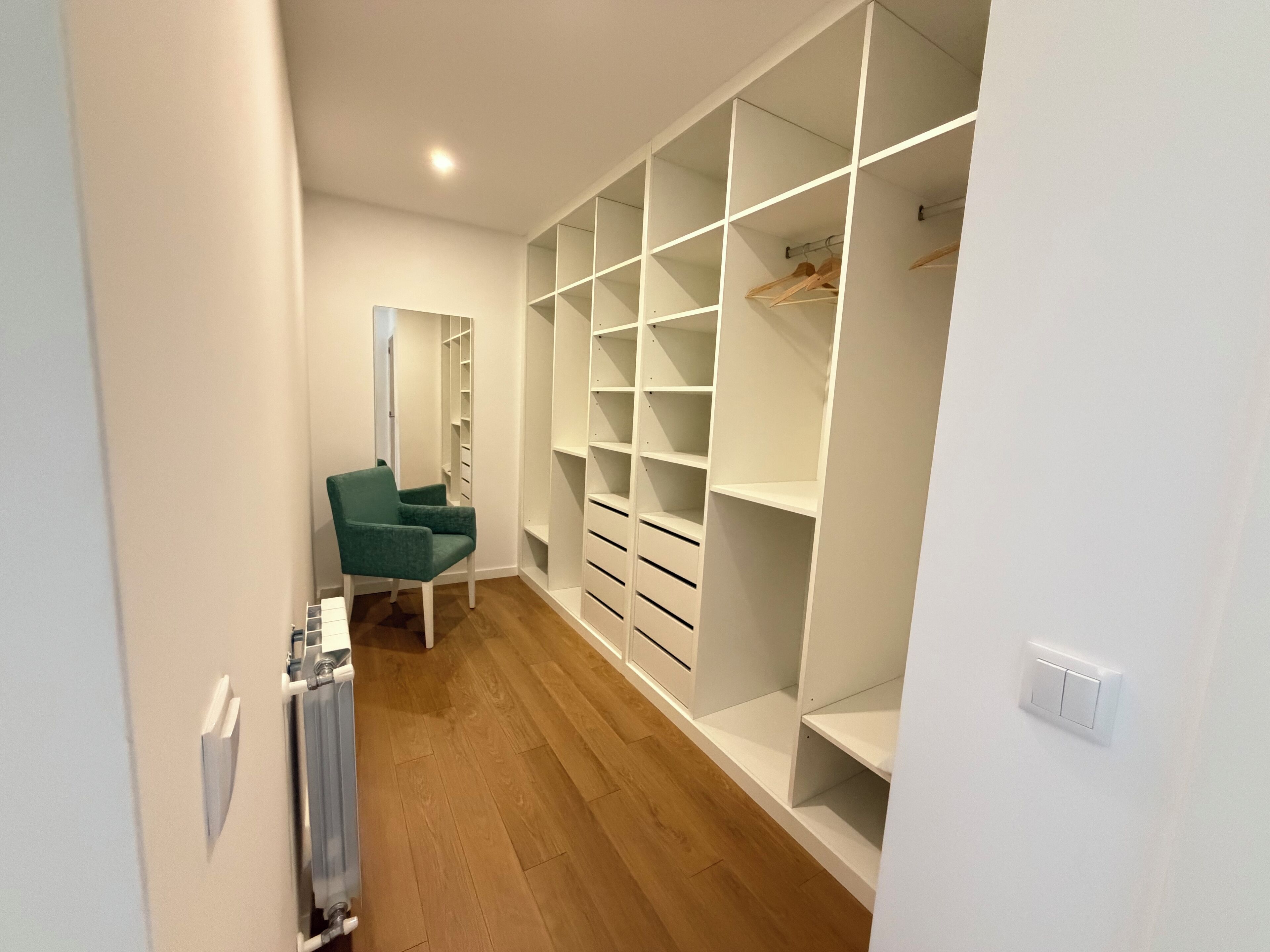 A walk-in closet with white shelving, a green chair, and a radiator.