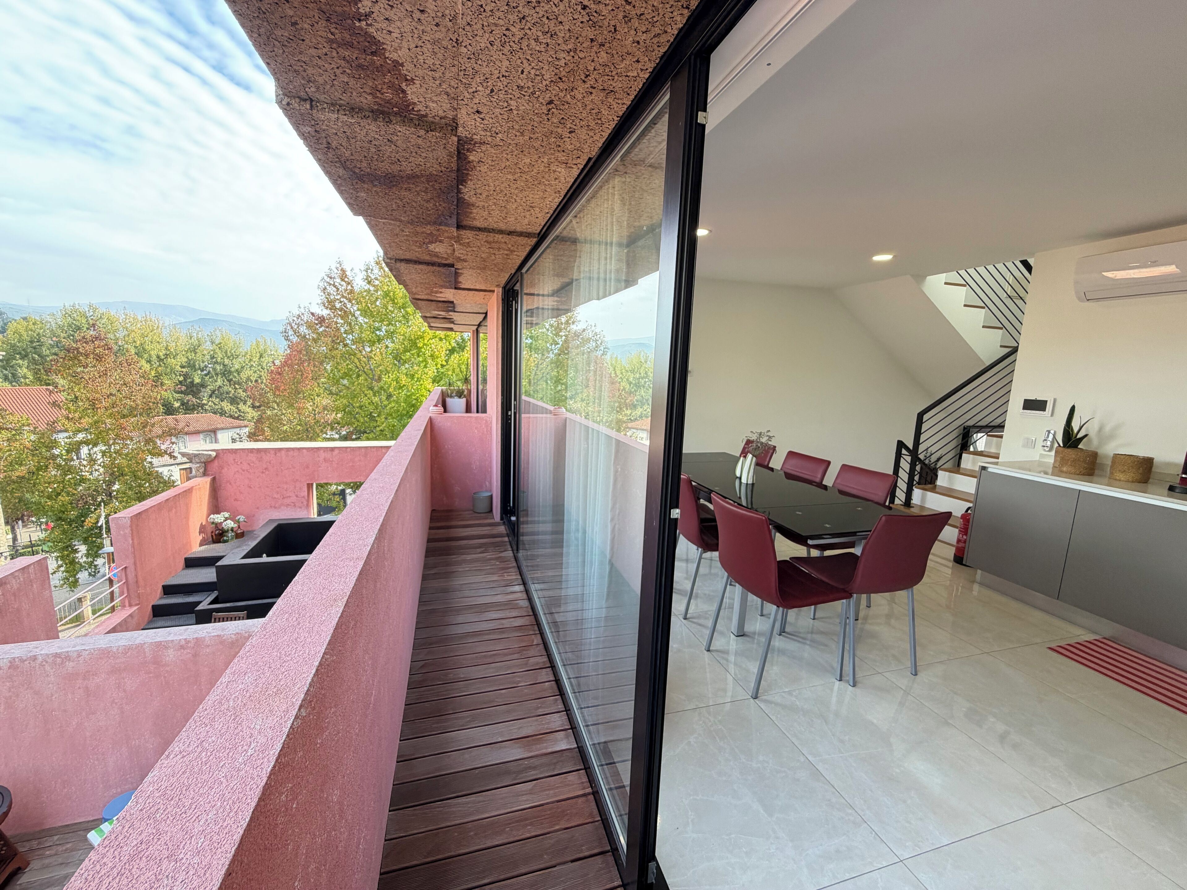 Een balkon met een houten vloer, een eettafel met stoelen en een keukenhoek met kastjes en een trap.