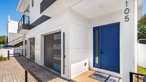 A modern two-story residential building with a blue door, a garage, and a visible number '105' on the facade. - Across The Beach • 4 Units • Sleeps 28 • Hot Tubs (Cocoa Beach)