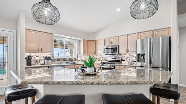 A modern kitchen with granite countertops, stainless steel appliances, and a central island with bar stools. - The Maverick Sunset Escape (Lake Havasu City)
