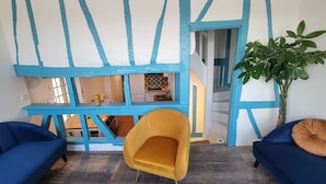 Ein Zimmer mit blauen und weißen Wänden, Holzboden und einem gelben Stuhl. Eine Treppe führt in ein weiteres Zimmer.