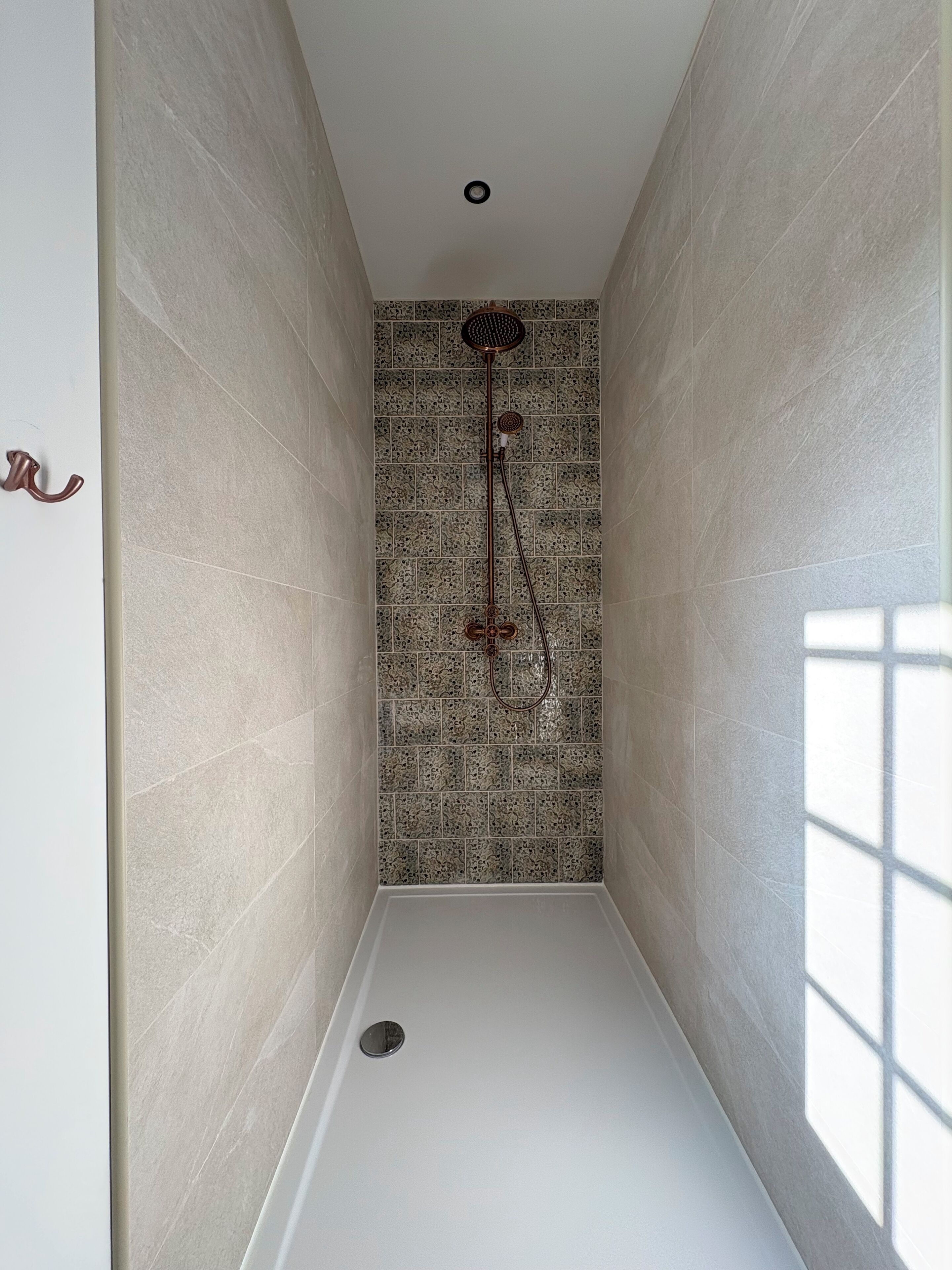 Un petit espace douche avec un mur carrelé, une pomme de douche et un drain.