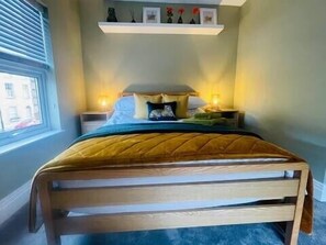 A bedroom with a bed, bedside tables, a window, and a shelf with decorative items. - Brazenose, Stamford, Lincolnshire. (Lincolnshire)