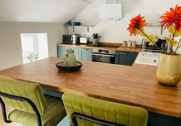 A modern kitchen with a wooden island, green upholstered chairs, and a vase with flowers. - Brazenose, Stamford, Lincolnshire. (Lincolnshire)