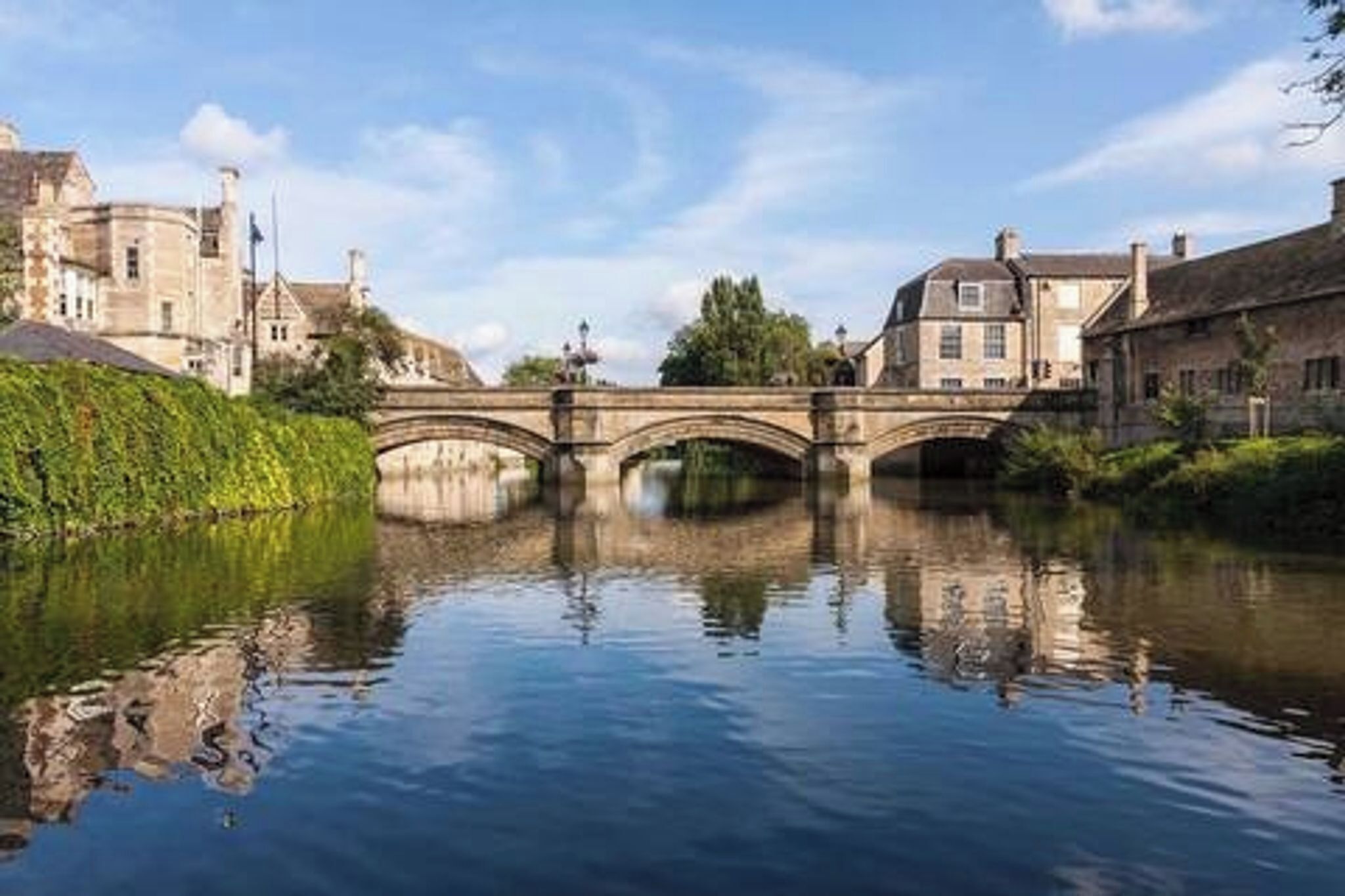 A stone bridge over a calm river with buildings on either side.