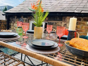 A table set with plates, glasses, and a candle, with a wicker chair in the foreground. - Brazenose, Stamford, Lincolnshire. (Lincolnshire)