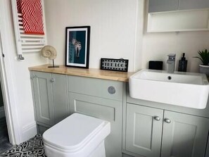 A bathroom with a white sink, a toilet, and a vanity with cabinets. There is a framed picture on the vanity and a decorative item on the countertop. - Brazenose, Stamford, Lincolnshire. (Lincolnshire)