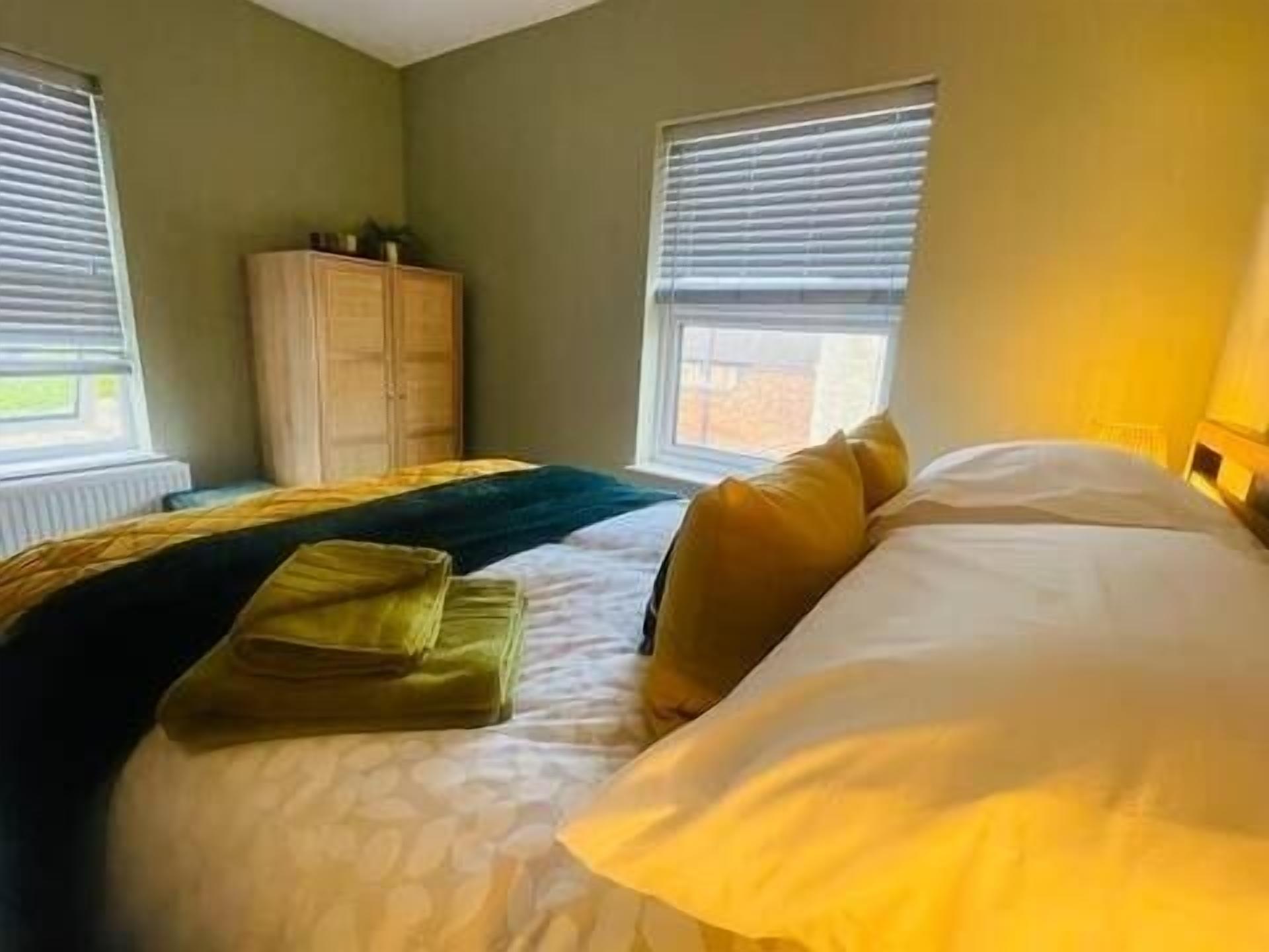 Een slaapkamer met een bed, twee ramen, een radiator en een kledingkast.