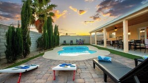 A backyard with a swimming pool, lounge chairs, and a covered patio area.