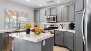 A modern kitchen with grey cabinets, stainless steel appliances, and a central island with a fruit bowl and flowers.