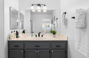 Een moderne badkamer met een grote spiegel, een wastafel en drie kastjes. Op het aanrecht liggen toiletartikelen en er is een handdoekrek met handdoeken.