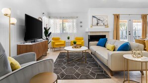 A modern living room with a flat-screen TV, yellow armchairs, a beige sofa, and a fireplace.