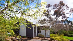 Une maison moderne à l’extérieur sombre, entourée d’une végétation luxuriante et d’arbres.