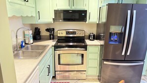 A kitchen with light green cabinets, stainless steel appliances including a refrigerator, oven, and microwave, and a sink with a faucet. - Beautiful serenity place (North Myrtle Beach)