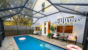 A backyard with a swimming pool, patio furniture, and umbrellas. - Walk to historic DOWNTOWN , Heated Pool, backyard Dining, grill, fire pit,Dog Ok (St. Augustine)