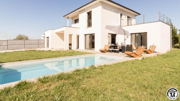 A modern two-story house with a swimming pool, outdoor seating, and a fenced yard.