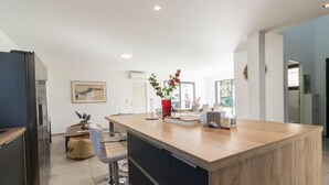 A modern kitchen with a large island, a dining area with chairs, and a view of the outdoors.