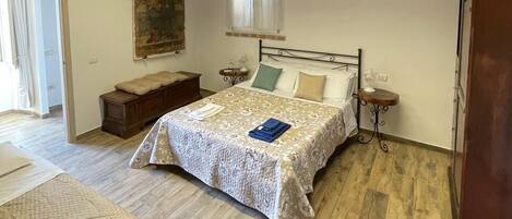 Quarto com teto de madeira, cama com colcha estampada, mesa de cabeceira com abajur e um banco de madeira.