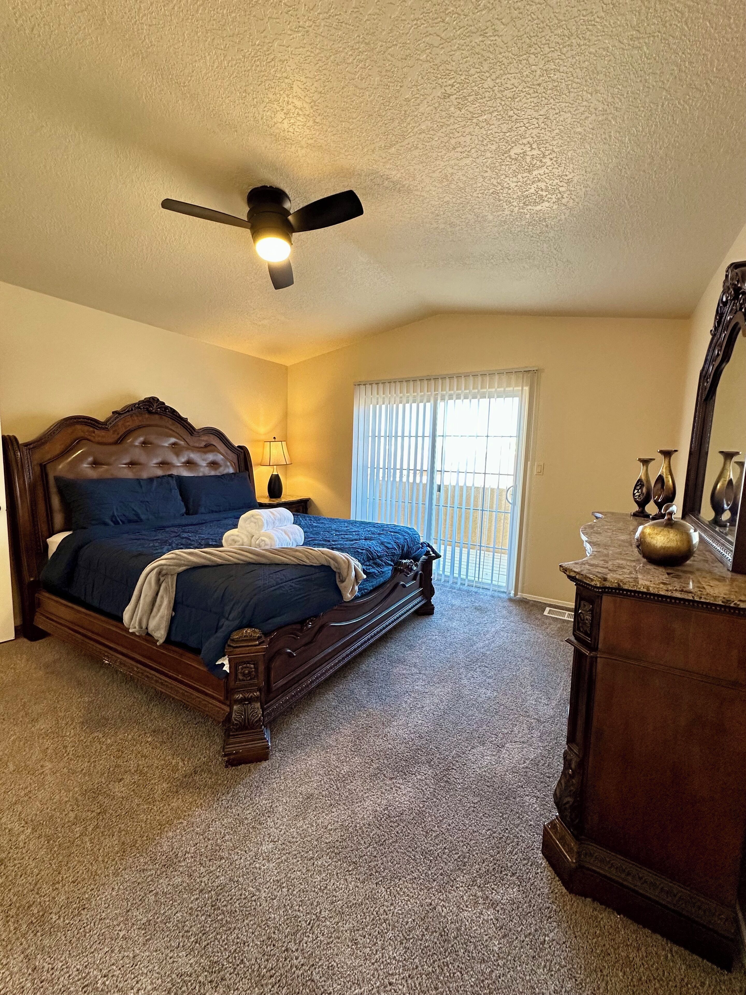 Quarto com uma cama grande, um ventilador de teto, uma janela com persianas e um penteado.