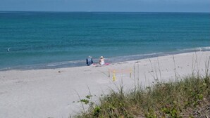 A beach with two people sitting on the sand, a volleyball net, and a clear view of the ocean.