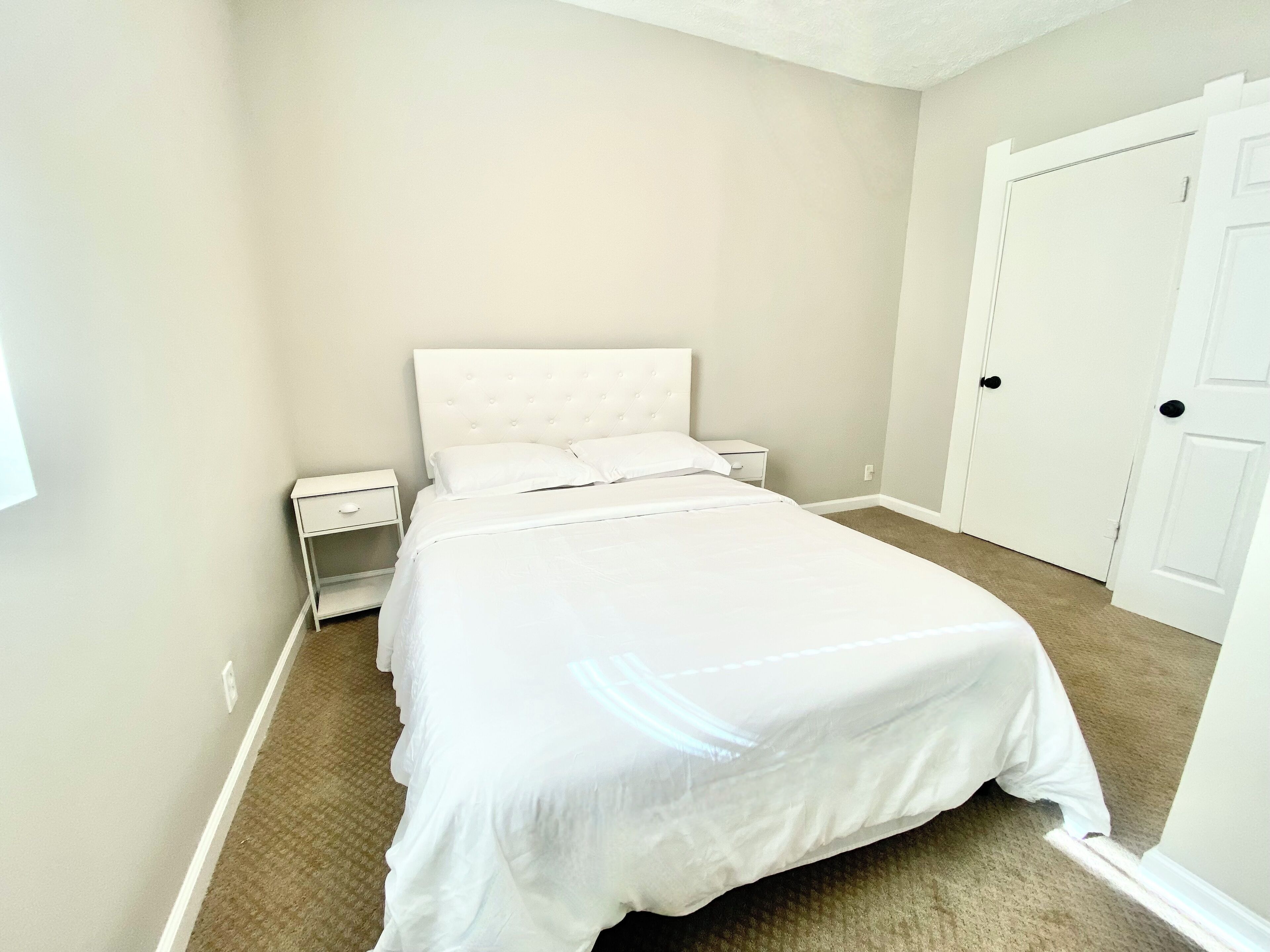 A bedroom with a large bed, a nightstand, a dresser, and a door.