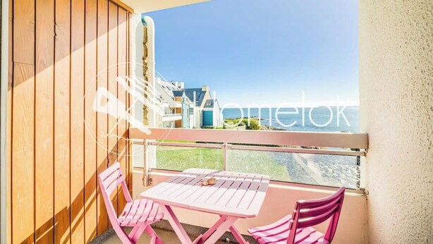 A balcony with a wooden fence, a pink table, and two pink chairs. - Appartement bord de plage, havre de paix (Ploemeur)