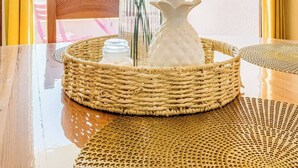 A table with a woven tray containing a vase with flowers and a white pitcher, set against a window with a view of a balcony. - Appartement bord de plage, havre de paix (Ploemeur)