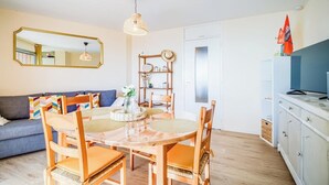 A living room with a dining table, chairs, a sofa, a mirror, and a bookshelf. - Appartement bord de plage, havre de paix (Ploemeur)