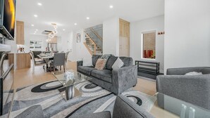 Un salon moderne comprenant un canapé, des fauteuils, une table basse en verre et un coin repas avec des chaises et une table.