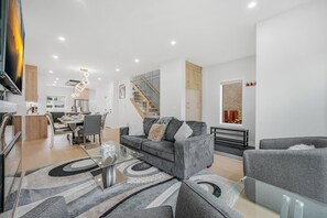 A modern living room with a sofa, armchairs, a glass coffee table, and a dining area with chairs and a table.