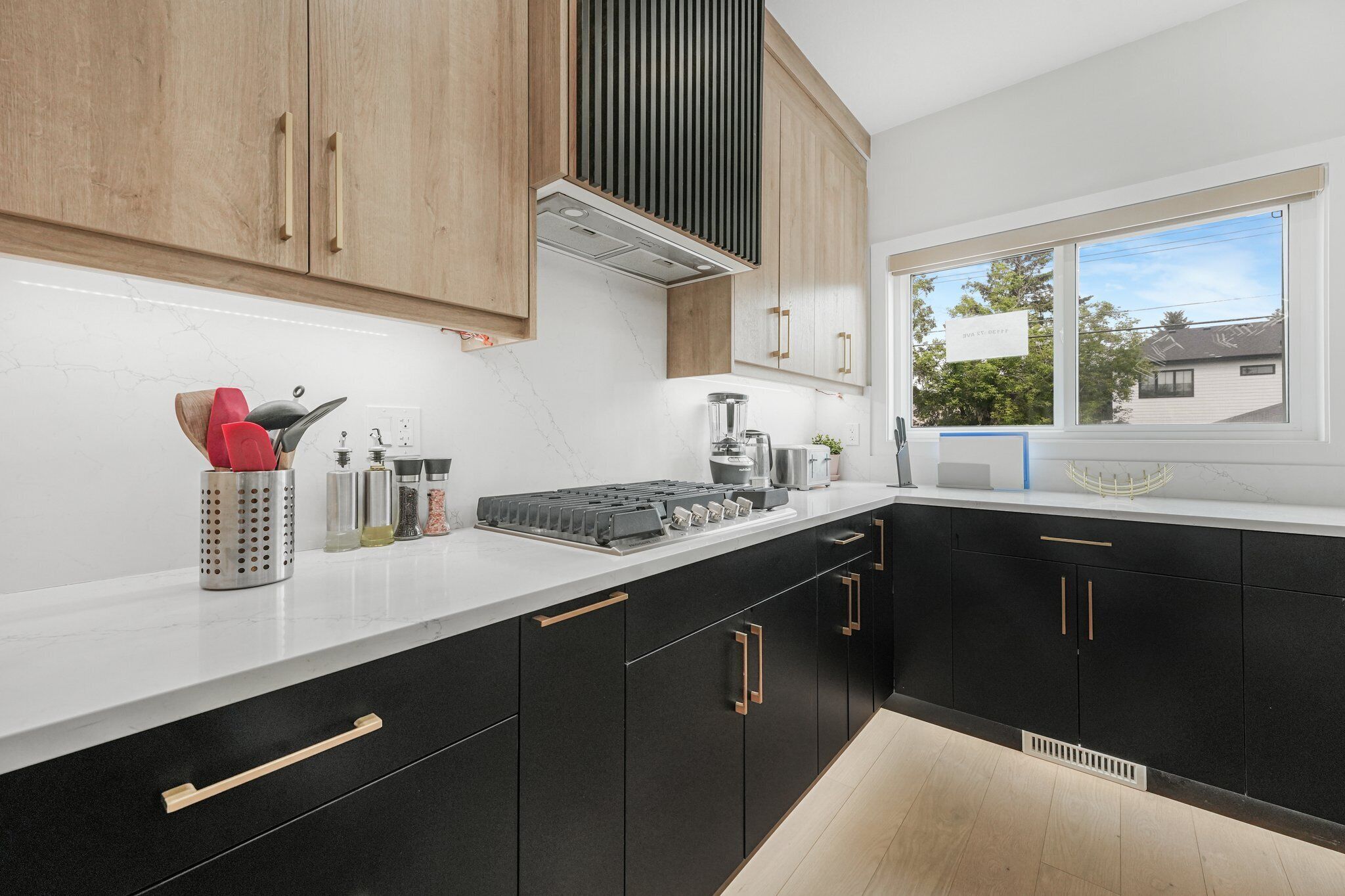 A modern kitchen with black cabinets, a white countertop, and a window with a view of houses.