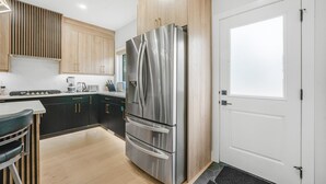 Une cuisine moderne avec un réfrigérateur en acier inoxydable, des armoires en bois et une porte blanche.