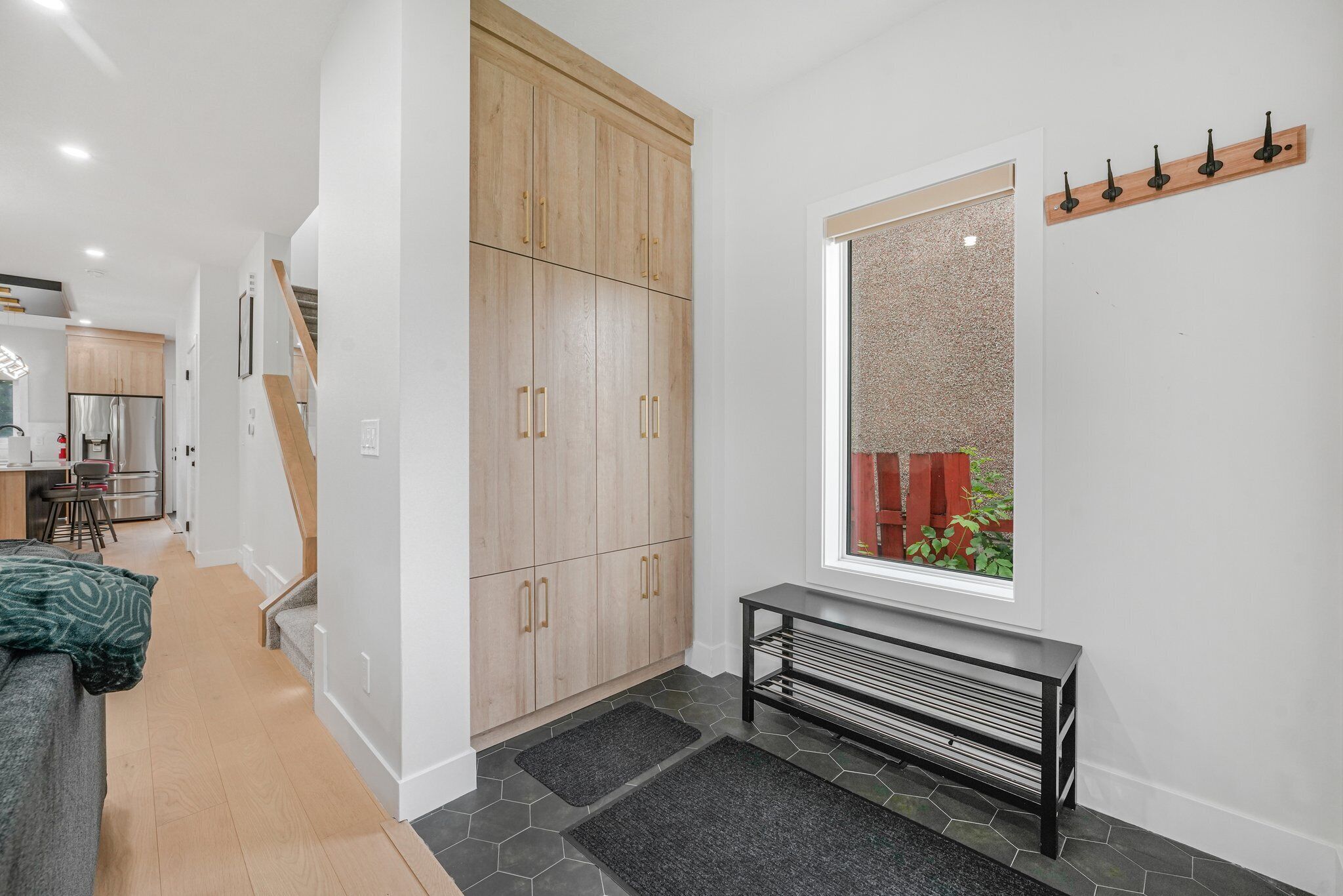 Un intérieur moderne avec une armoire en bois, un banc et une fenêtre donnant sur une clôture rouge.