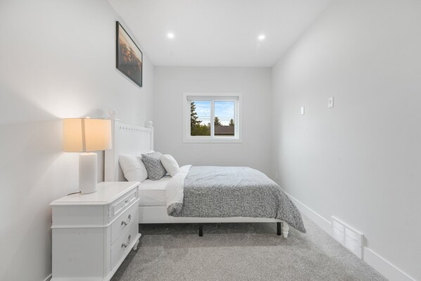 A bedroom with a bed, a bedside table, a lamp, a window, and a picture on the wall.