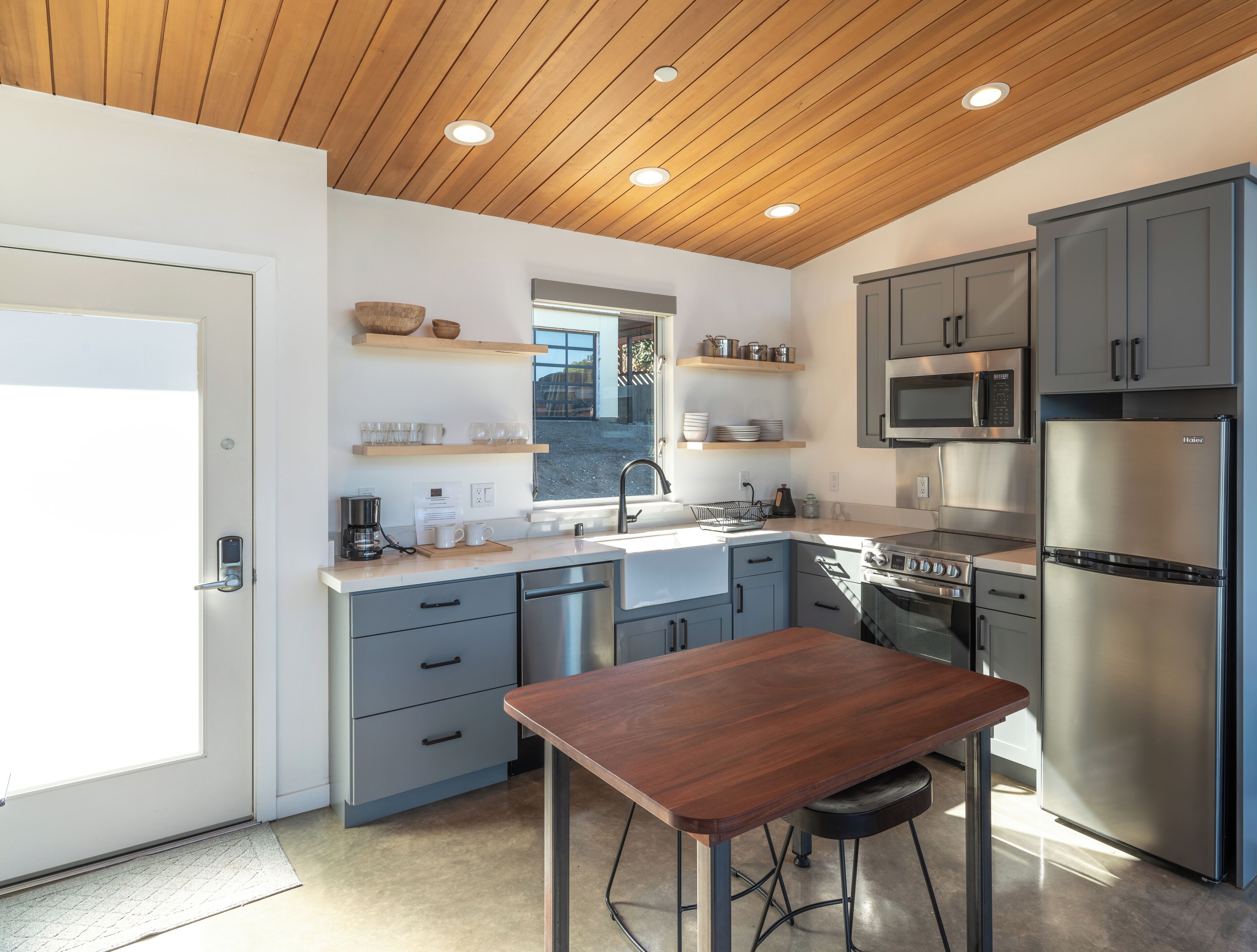 A modern kitchen with grey cabinets, stainless steel appliances, and a wooden ceiling.