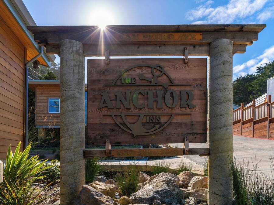 A wooden sign for The Anchor Inn with a clear view of the surrounding area, including a building and a wooden fence.