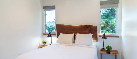 Un dormitorio con una cama grande, dos mesitas de noche, un cabecero de madera y dos ventanas con persianas.