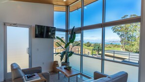 A modern living room with a large window, a flat-screen TV, a sofa, a coffee table, and a potted plant. - anchor inn pacifica (Pacifica)