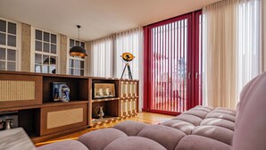 A modern living room with a large sectional sofa, wooden shelving with decorative items, and a large window with red blinds. - Villa T5 - Pool - Casa da Brêa Viana do Castelo (Santa Marta de Portuzelo)