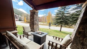 A covered patio with a stone pillar, a fire pit, and two wooden sofas with cushions.