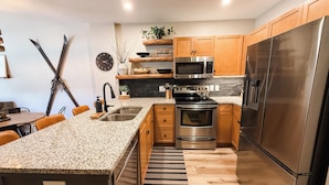 A modern kitchen with granite countertops, stainless steel appliances, wooden cabinets, and a black and white striped rug.