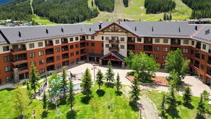 A large, multi-story hotel with a central courtyard, surrounded by lush greenery and a mountain backdrop.